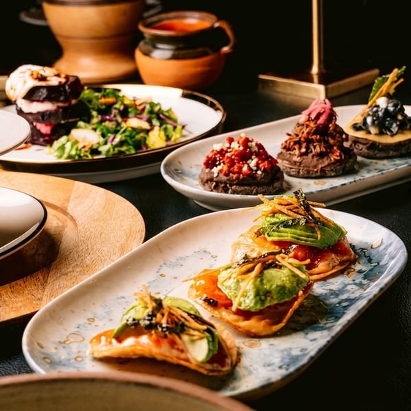A table laden with various small plates of gourmet food, including salads, tostadas, and desserts.