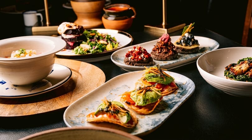 A table laden with various small plates of gourmet food, including salads, tostadas, and desserts.