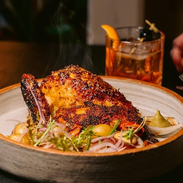 Steaming roasted chicken with vegetables and a cocktail, with a hand reaching for a fork.