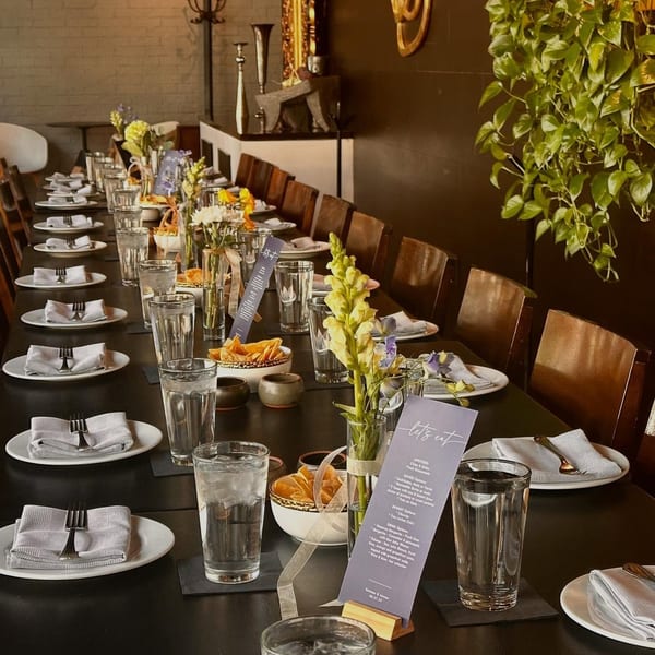 A long dining table set for a private event with place settings, flowers, and menus.