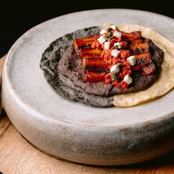 Pork belly with red sauce, black beans, and cheese on a tortilla, with green salsa.