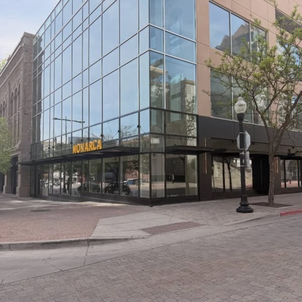 Exterior view of Monarca restaurant, a modern building with large glass windows and a brick sidewalk.
