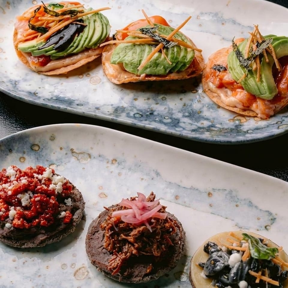 Two plates of gourmet Mexican sopes and tostadas with various toppings like avocado, beans, and meat.
