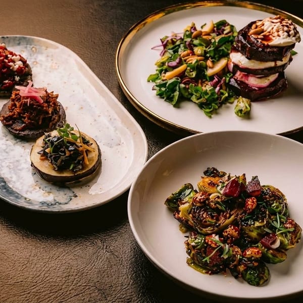 Three plates of gourmet dishes, including beet and goat cheese stacks, and roasted Brussels sprouts.